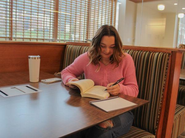 Laci Thompson sitting at a table writing on a book